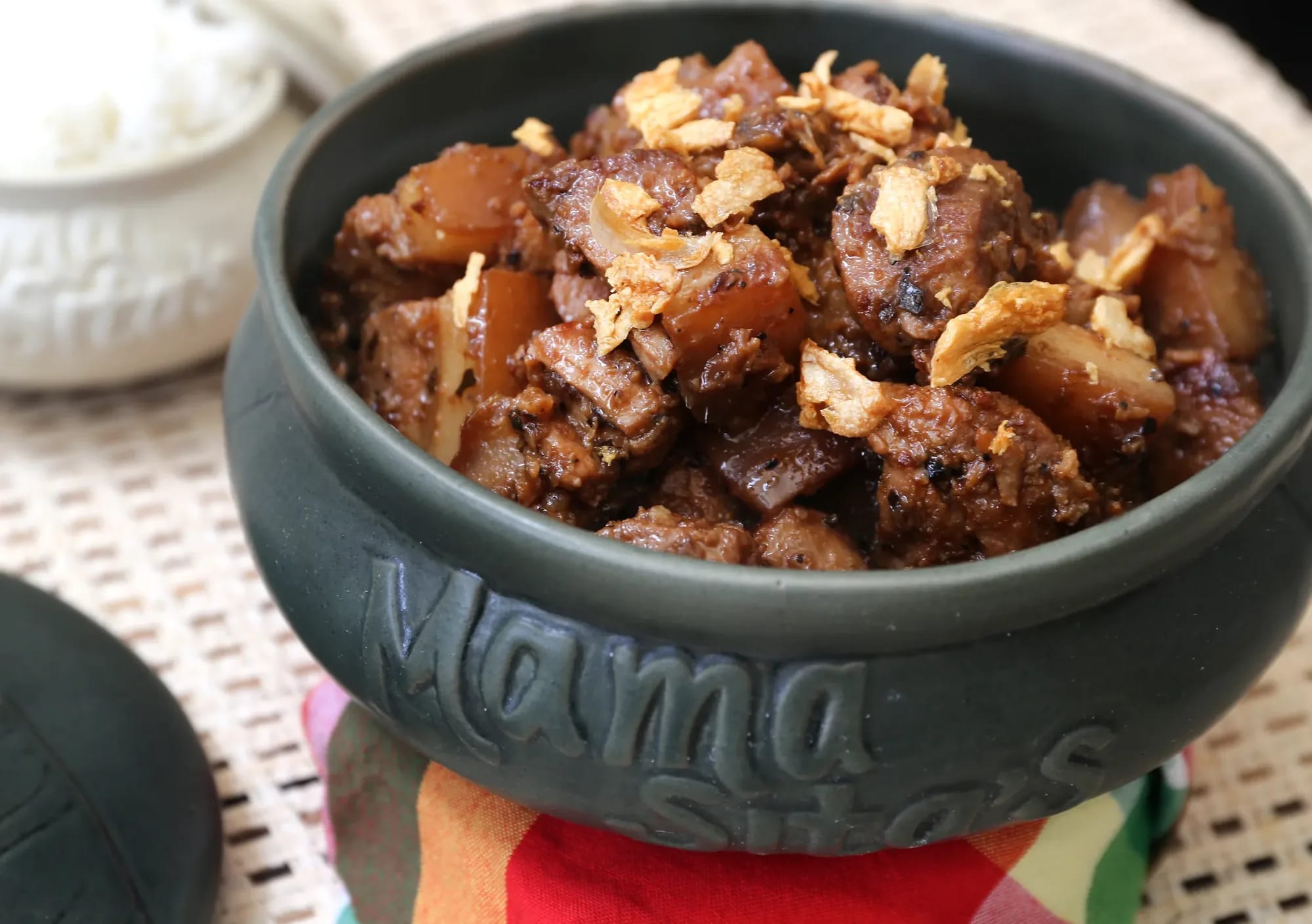 Pork adobo topped with fried garlic in a stone bowl embossed with the Mama Sita's name