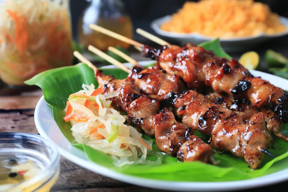 Grilled chicken barbecue skewers plated on a banana leaf with atsara