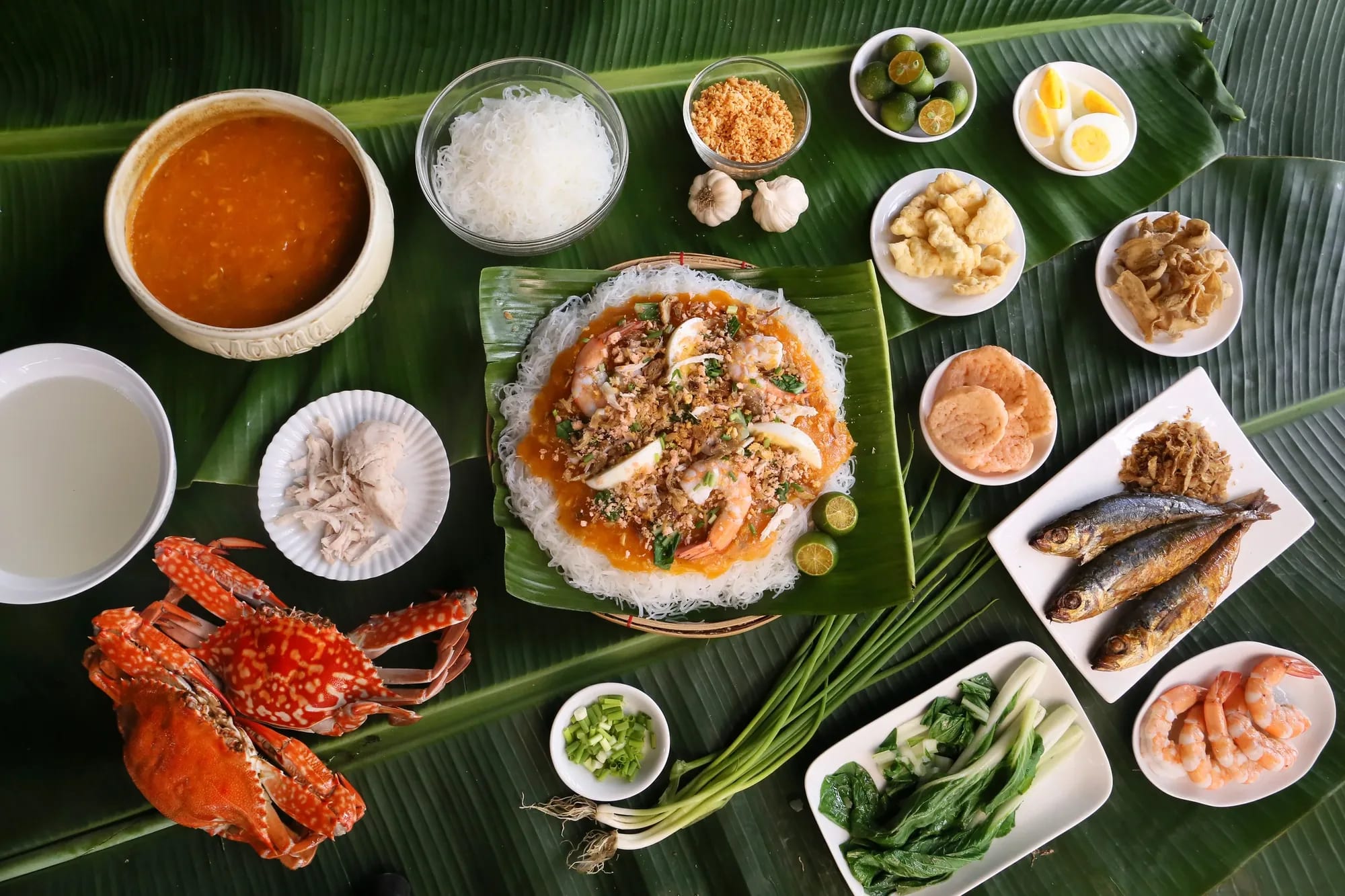 A palabok spread laid out on banana leaves with crab, shrimp, tinapa and small bowls of sawsawan